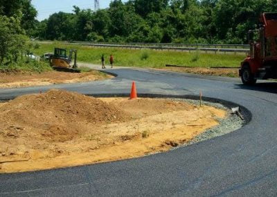 Construction site with asphalt paving equipment and a curve in a newly paved road in Frederick, Maryland, surrounded by greenery and traffic barriers.