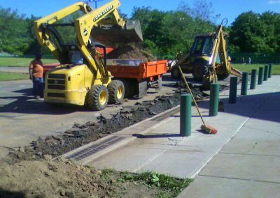 Two backhoes digging pavement in Frederick while a worker observes; one backhoe loads a dump truck with dirt during an asphalt paving project in Maryland.