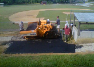 Workers from a Frederick paving contractor operate machinery to lay asphalt on a pathway near a baseball field in Maryland.