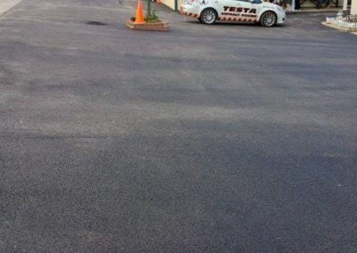People waiting in line outside a building with a large paved parking lot, recently finished by a Maryland asphalt paving company, and a small car parked nearby.