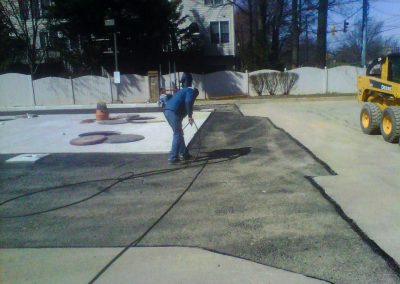 A paving contractor from an asphalt paving company in MD is using power tools to lay asphalt in front of a building on a sunny day.