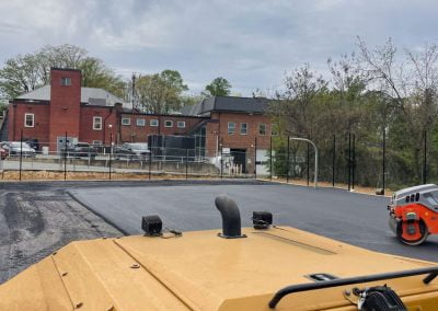 Yellow construction equipment from an asphalt paving company is positioned on a newly paved area, with a row of brick buildings and parked cars in the background. This scene showcases the precision and quality associated with construction work in Maryland (MD).