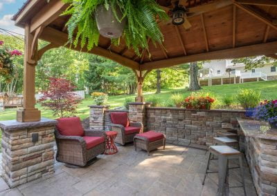 A cozy patio with wicker furniture under a wooden pergola, a stone bar, and a lush garden with colorful flowers awaits you in Frederick, Maryland.