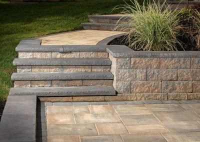 Stone steps leading up to a curved path bordered by a retaining wall and grass plant landscaping, expertly crafted by a renowned paving contractor in Maryland.