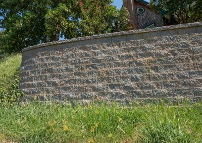 Stone retaining wall with green grass in the foreground, trees, and a house in the background, typical of picturesque Maryland landscapes.