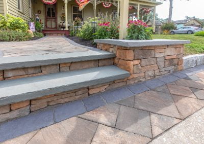 Stone pathway and steps leading to a house with a flower bed and porch in the background, typical of charming Maryland homes. Consider an asphalt paving company in MD for enhancements that blend seamlessly with the natural beauty.
