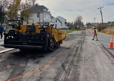 A road construction crew in Frederick, MD is working with heavy machinery on an asphalt paving project near residential houses.