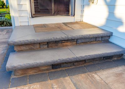 Concrete steps lead up to a doorway, surrounded by a patio with large square and rectangular stone tiles, common in Frederick, Maryland.