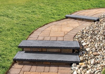A curved stone path with steps, bordered by green grass and decorative rocks, crafted by a skilled Maryland paving contractor.
