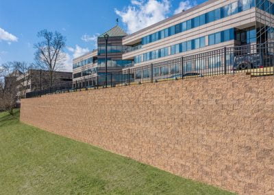 Office building with large retaining wall and grassy slope, under a blue sky with clouds, expertly designed by a top asphalt paving company.