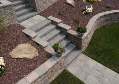 Stone steps and retaining walls in a landscaped garden, expertly crafted by a renowned paving contractor, with plants and flowers in pots and beds.