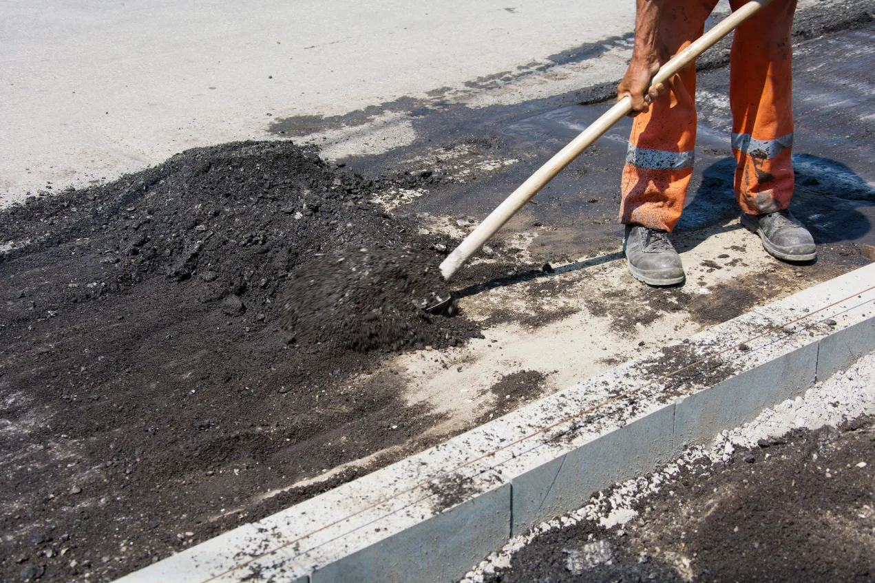 asphalt-millings-1 Worker in orange gear spreading asphalt with a shovel on a road.