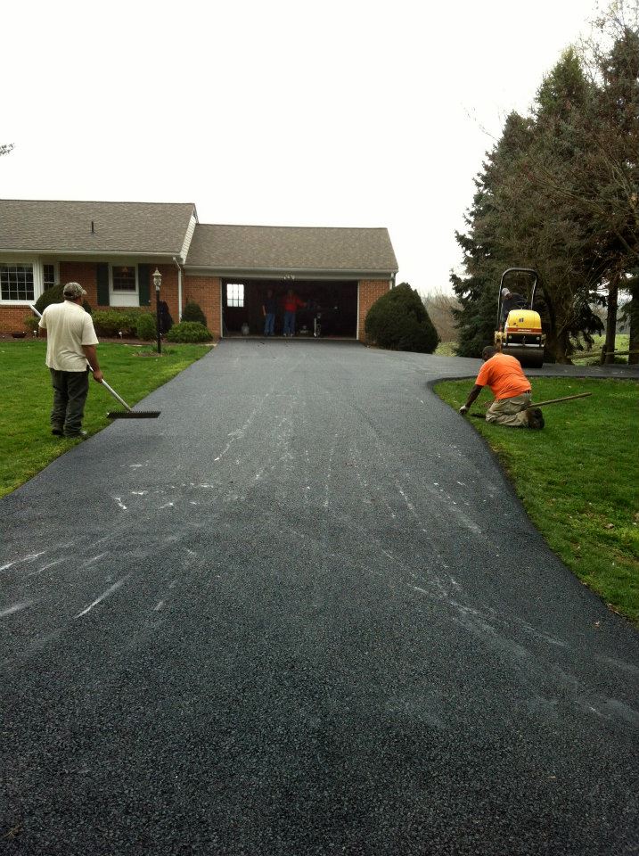 522155_365286770246441_1208461923_n Two workers smooth newly paved asphalt on a driveway leading to a house with an open garage.