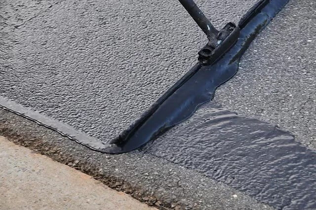 Asphalt-Sealcoating-Photo1-1 A squeegee spreads fresh black sealcoat onto an asphalt driveway, covering old gray pavement.