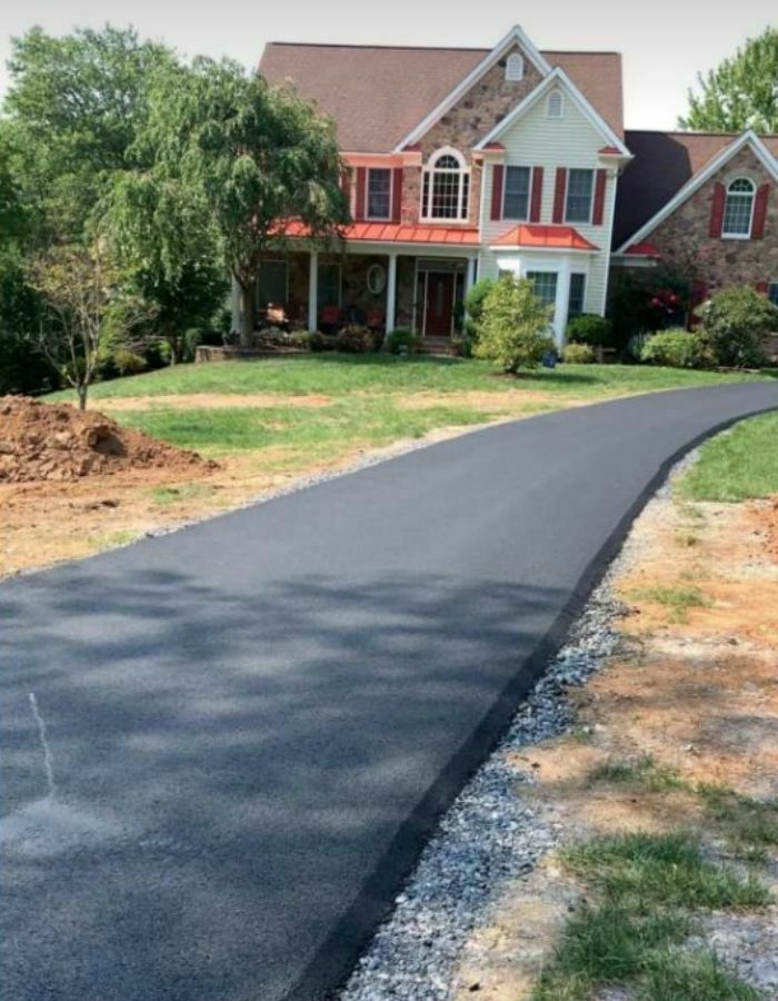 Freshly paved asphalt driveway leading to a large house with a red roof and stone exterior.
