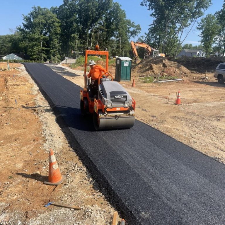 Copy-of-ceemitemplate-800-800-3-768x768 A worker operates a road roller on freshly paved asphalt at a construction site with trees in the background.