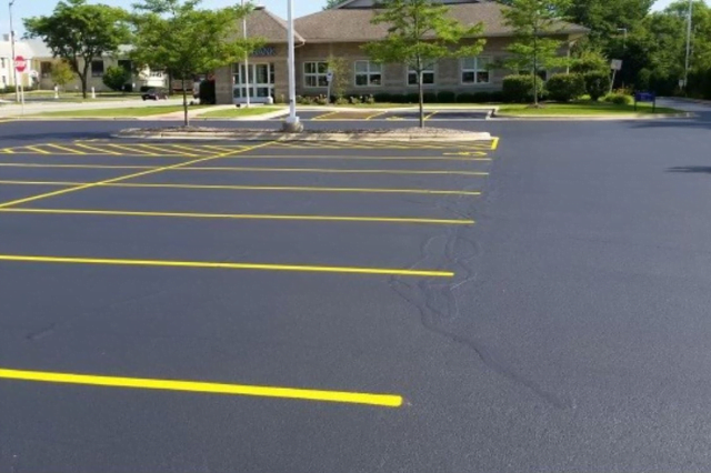 Untitled-design-71 Freshly paved and striped empty parking lot with a building and trees in the background.