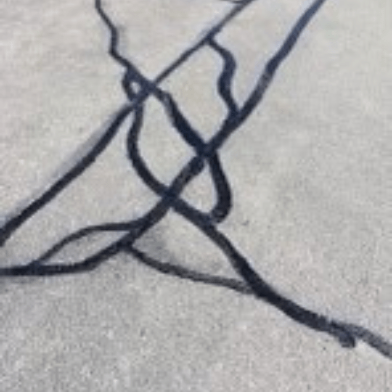 Black tar lines fill cracks on a gray concrete surface, creating an abstract, intersecting pattern.