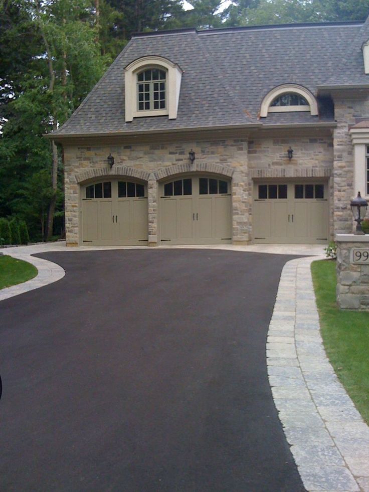 driveway Large stone house with three arched garage doors and a curved paved driveway in front.