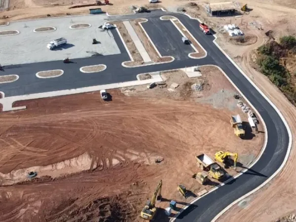Aerial view of a construction site with heavy machinery and newly paved roads on dirt ground.