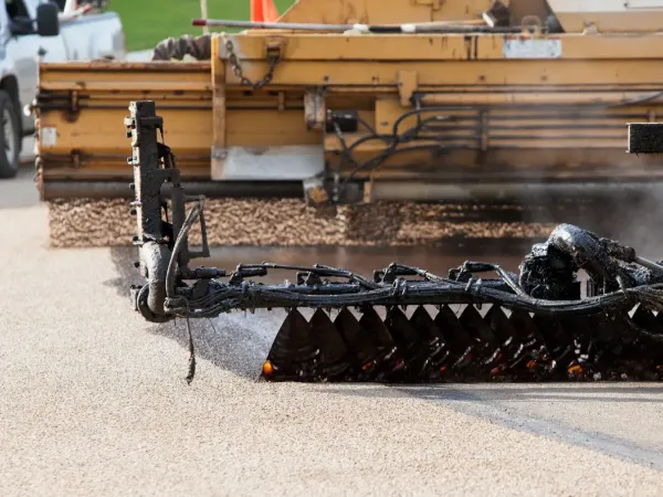 Close-up of road paving equipment applying hot asphalt to a street during construction.