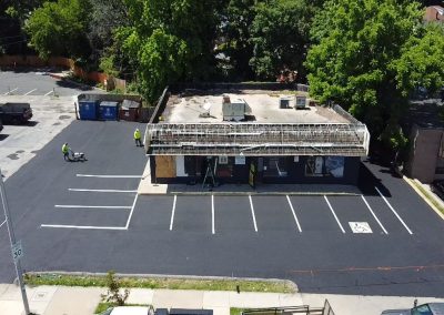 Aerial view of a small building with a newly paved, mostly empty parking lot and two workers in safety vests.