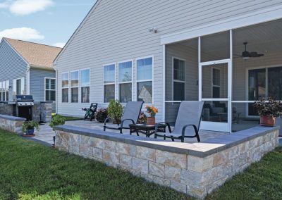 Backyard patio with lounge chairs, potted plants, grill, and a screened porch attached to a beige house.