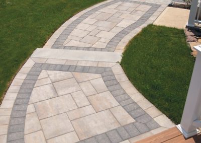 Curved stone walkway with gray borders set in green grass, leading away from a wooden porch.