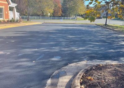 Empty asphalt parking lot with tree shadows, a curb, and autumn trees in the background under a clear sky.