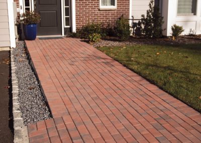 Red brick walkway leading to a front door, with gravel edging and a grassy lawn on the right.