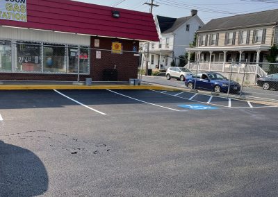Small brick store with a red roof and empty parking spaces, including a marked accessible spot in front.