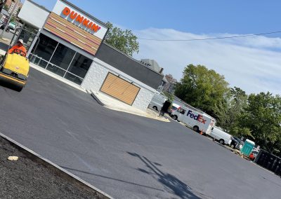 A newly paved parking lot outside a Dunkin’ store, with a FedEx truck parked nearby on a sunny day.