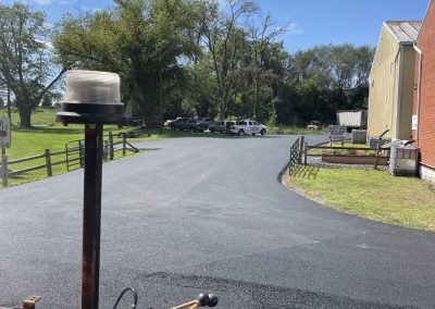 Freshly paved driveway under a blue sky, with trees and buildings in the background.