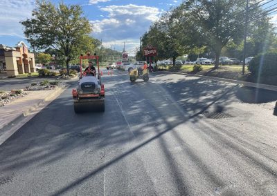 Two workers operate steamrollers to pave a road near a Wendy's restaurant on a sunny day.