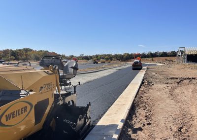 Yellow paving machine laying fresh asphalt on a new road under a clear blue sky at a construction site.