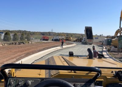 View from inside a construction vehicle facing a roadwork site with workers and trucks under a clear sky.