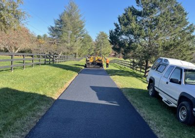 A newly paved asphalt driveway with a truck and worker in the distance on a sunny day.