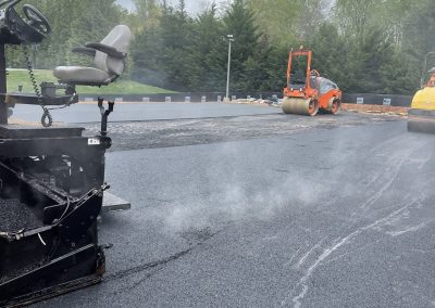 Steam rises from freshly paved asphalt as construction vehicles smooth the surface on a cloudy day.