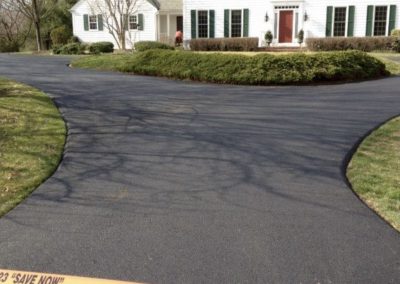 Freshly paved black driveway in front of a white house, blocked off by a "Testa Asphalt Paving" caution tape.