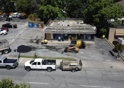 Aerial view of a parking lot under construction, with vehicles, equipment, and workers near a small building.