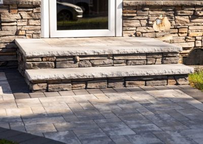 Two stone steps lead to a door, with a paved stone walkway and a small "grateful" sign on the right.