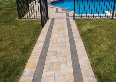 Stone walkway leads to an open gate and a fenced, in-ground swimming pool in a grassy backyard.