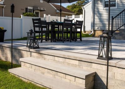 Outdoor patio with black table, chairs, umbrella, lanterns, and steps leading to a grassy backyard.
