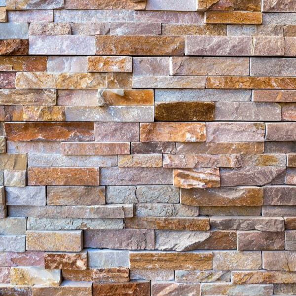 A close-up of a wall made of variously sized, stacked, rectangular stone bricks in earthy tones.