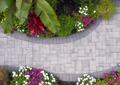Aerial view of a stone garden path bordered by colorful flowers, green shrubs, and large leafy plants.
