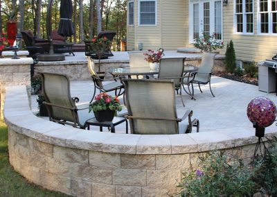 Backyard patio with metal chairs and tables, surrounded by a stone wall, next to a yellow house.