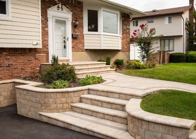 Curved stone steps and retaining wall leading to a white front door of a suburban brick house.