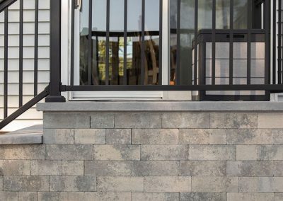 Stone porch with black metal railing and sliding glass door, next to light gray siding.