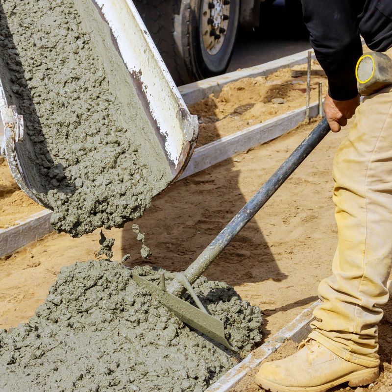 wgt-img2-7-min Wet concrete is poured from a chute as a worker spreads it with a shovel on a construction site.